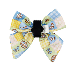 The Sassy Woof Dog Sailor Bow - Patch Perfect features a colorful patchwork design with rabbits, bows, and flowers in blue, yellow, and green squares. It includes a black center band and a small white tag.