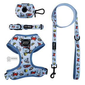 The Sassy Woof Dog Four Piece Bundle - Coastal Cuties includes a light blue adjustable harness, collar, leash, and waste bag holder with a nautical crab, sailboat, and seashell pattern.