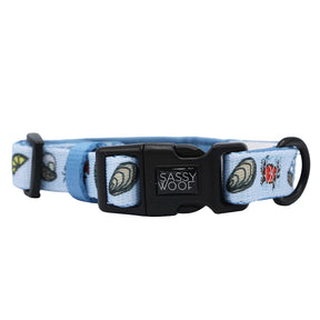 The Sassy Woof Dog Collar – Coastal Cuties features light blue fabric with seashell and ladybug designs, a black clasp, and D-ring—ideal for fans of coastal dog accessories.