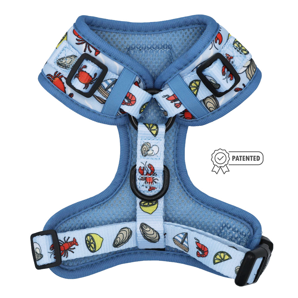 The Sassy Woof Dog Adjustable Harness - Coastal Cuties features blue mesh with crabs, seashells, sailboats, and lemon slices, plus black buckles and straps. A Patented badge appears next to the harness.