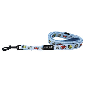 The Sassy Woof Dog Leash - Coastal Cuties is light blue with colorful seafood prints and a black clip. It matches the adjustable harness and features a signature Sassy Woof label for extra charm.
