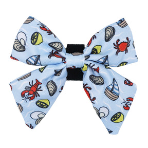 The Sassy Woof Dog Sailor Bow - Coastal Cuties features a playful light blue design with red lobsters, crabs, mussels, lemon slices, and sailboats.