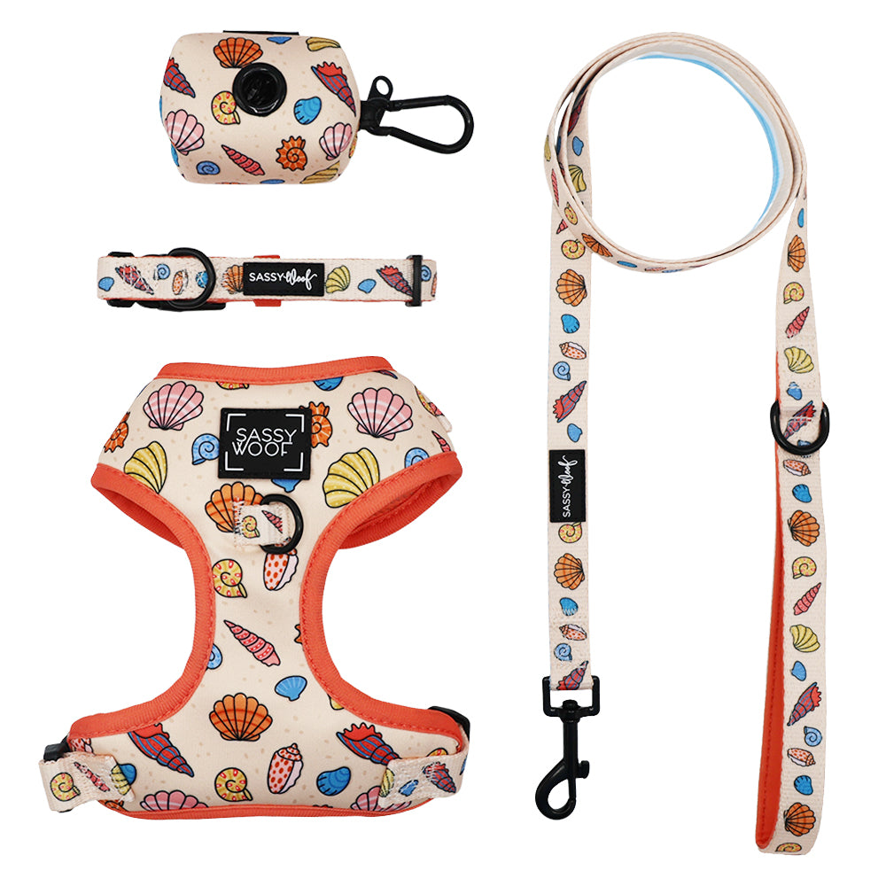 The Sassy Woof Dog Four Piece Bundle - Shell Yeah includes a seashell-patterned harness with orange trim, collar, leash, and waste bag holder—perfect for seaside strolls in colorful ocean style.