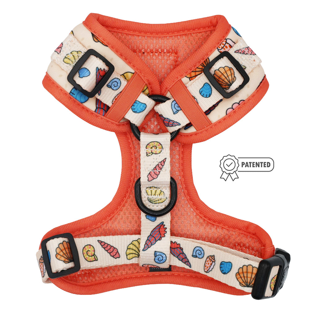 The Sassy Woof Dog Adjustable Harness - Shell Yeah features a beige and orange ocean-themed design with seashell prints, black adjustable buckles for growing pups, and a patented badge on the right side.
