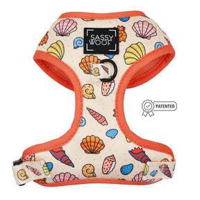 The Shell Yeah Dog Adjustable Harness by Sassy Woof features a colorful seashell pattern, orange trim, front logo patch, puppy growth protection, and a patented badge on the right side.
