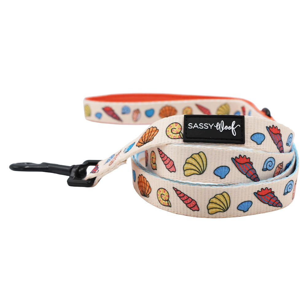 The Sassy Woof Dog Two Piece Bundle - Shell Yeah features a beige leash with seashell and conch designs, a black metal clip, and SASSY WOOF patch—ideal for pairing with beach dog accessories or an adjustable harness.