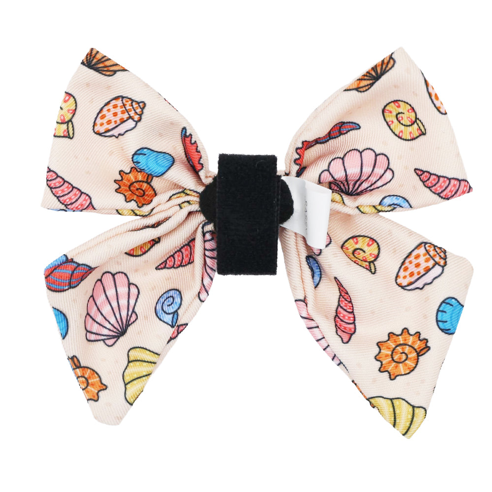 The Sassy Woof Dog Sailor Bow - Shell Yeah features a colorful seashell and starfish print, a black center band, and a small white tag—perfect for pairing with your favorite beachy dog collar or seashell accessories.