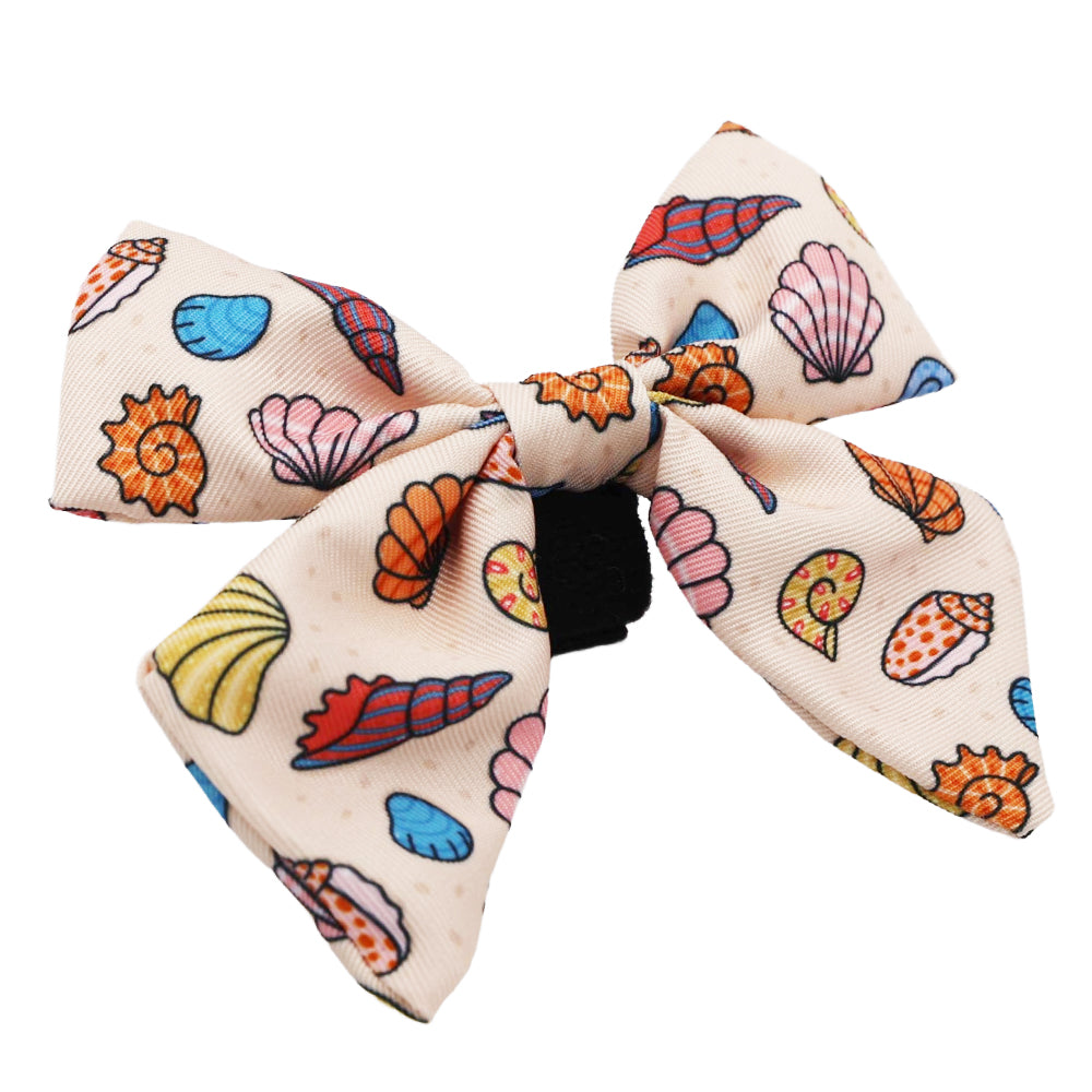 The Sassy Woof Dog Sailor Bow - Shell Yeah features a cream fabric with colorful seashells in orange, pink, blue, and yellow on a black hair tie—a fun accessory for your pup or to match their beachy dog collar.