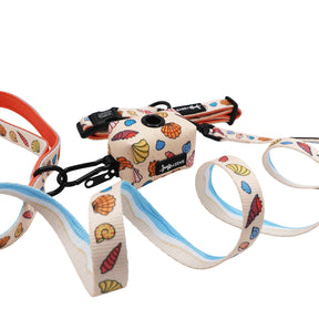 The Sassy Woof Dog Three Piece Bundle - Shell Yeah features a collar, leash, and waste bag holder with a colorful seashell print—coiled leash in front, other pieces behind—for pups on their puppy growth pawtection plan!.