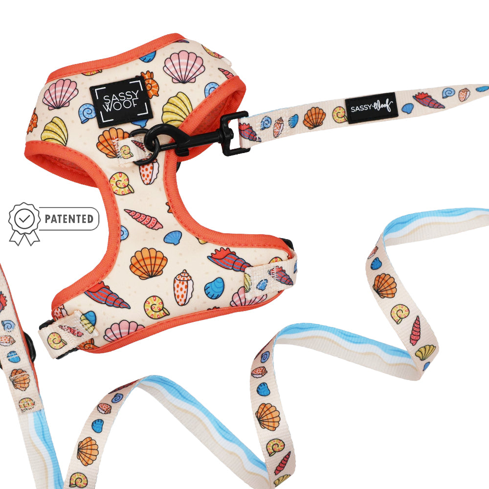 The Sassy Woof Dog Two Piece Bundle - Shell Yeah is a cream-colored adjustable harness and leash set with orange trim, featuring colorful seashell and ocean-themed designs—perfect for your beach-loving pup.