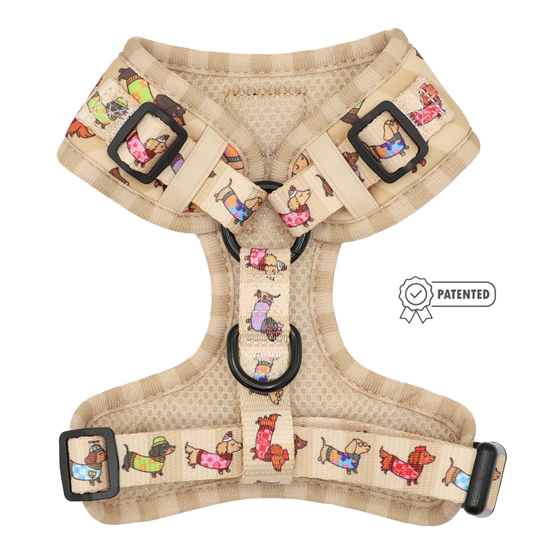 The Sassy Woof Dog Adjustable Harness - Sunbean features a beige base adorned with vibrant cartoon dog illustrations, complemented by black buckles and adjustable straps. This no pull harness is designed for optimal comfort and control during walks. A Patented badge appears to the right of the harness.