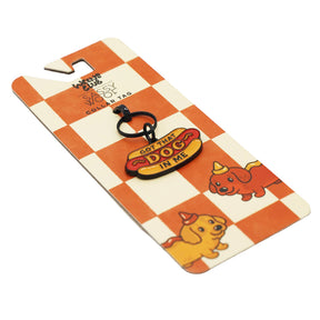 The "Collar Tag - Hot Dawg" by Sassy Woof is a hot dog-shaped keychain tag with "GOT THAT DOG IN ME" text, attached to a card featuring cartoon dogs in party hats on a red-and-white checkerboard background.