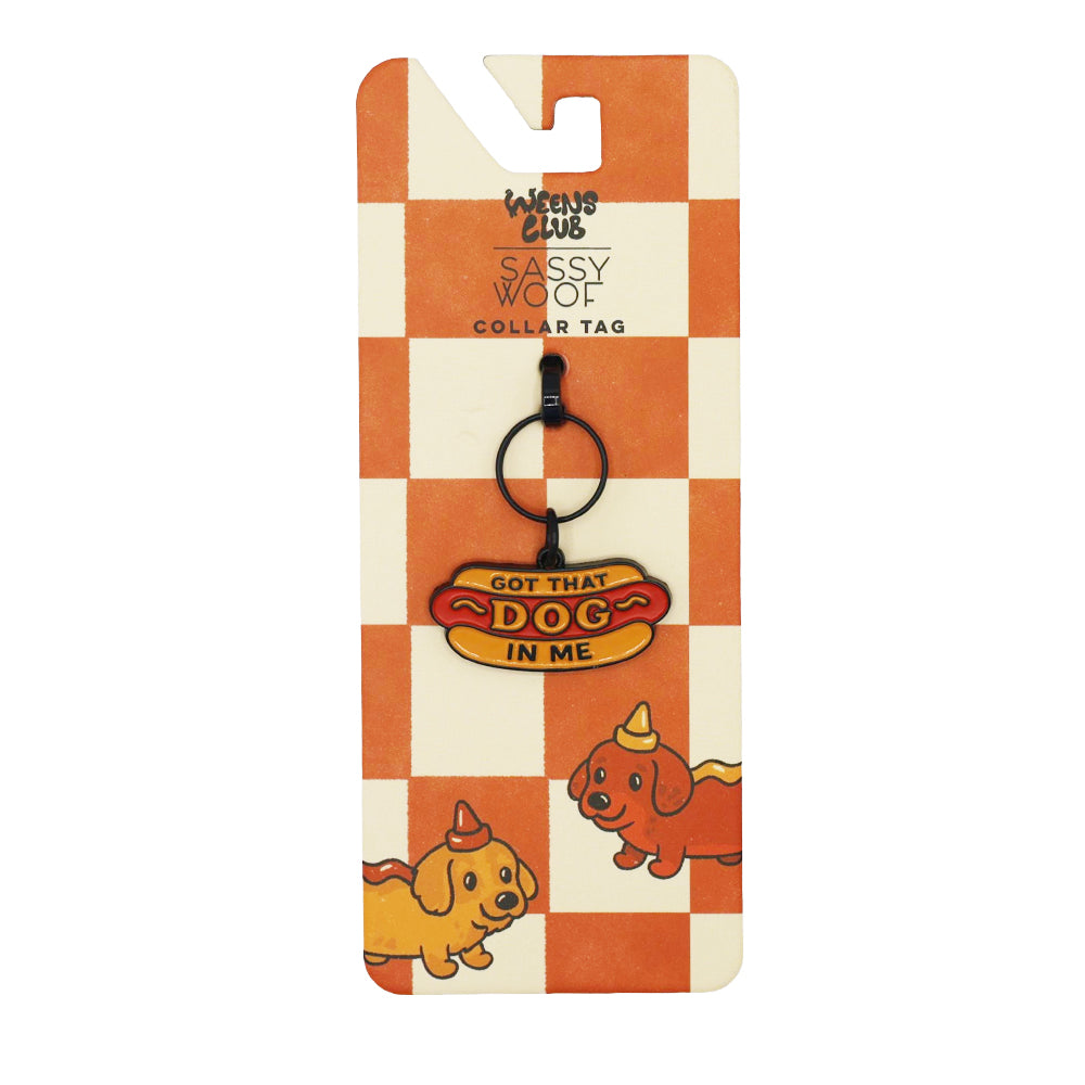 The Sassy Woof Collar Tag - Hot Dawg is a dachshund-shaped charm with “Got That Dog In Me” on orange and white checkered packaging featuring illustrated dogs in party hats from the weenie inspired collection.
