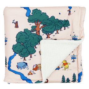 The Sassy Woof Pet Blanket – Disney's Winnie the Pooh features soft fabric with Winnie the Pooh characters and trees on a light background, plus a cozy white sherpa lining revealed on a folded corner.