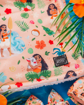 The Sassy Woof Pet Blanket – Disney's Moana features a peach backdrop with Moana, Pua, leaves, flowers, and coconuts, framed by orange flowers and palm leaves—an ideal match for any Disney Moana dog harness.