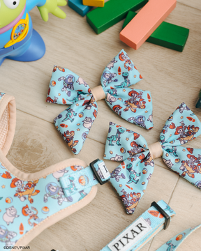 Two Dog Sailor Bows by Sassy Woof, featuring Disney and Pixar's Toy Story prints, rest beside a matching adjustable harness and collar—fun Pixar-branded accessories for your pup's next trip to the dog park.