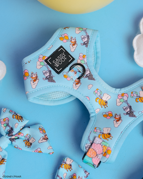 A blue adjustable dog harness—Sassy Woof’s Disney and Pixar's Up design—rests on a blue surface with matching accessories and white cloud shapes, featuring playful patterns inspired by the beloved movie.