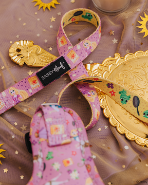 A pink and purple Sassy Woof dog leash featuring Disney's Rapunzel is displayed on gold star tulle with gold sun and flower accents, alongside a Rapunzel-themed mirror and hairbrush.