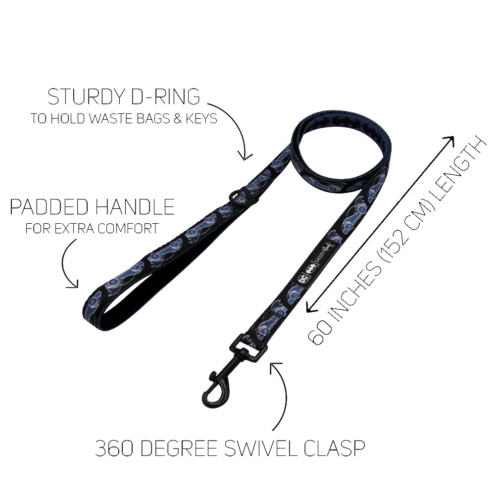 Certainly! Here’s a revised version of the sentence incorporating your product data: Black dog leash with a blue pattern from the Sassy Woof Dog Collar Three Piece Bundle – Batman™, featuring a sturdy D-ring for bags and keys, a padded handle, 60-inch (152 cm) length, and a 360-degree swivel clasp. Arrows highlight each feature on a white background.