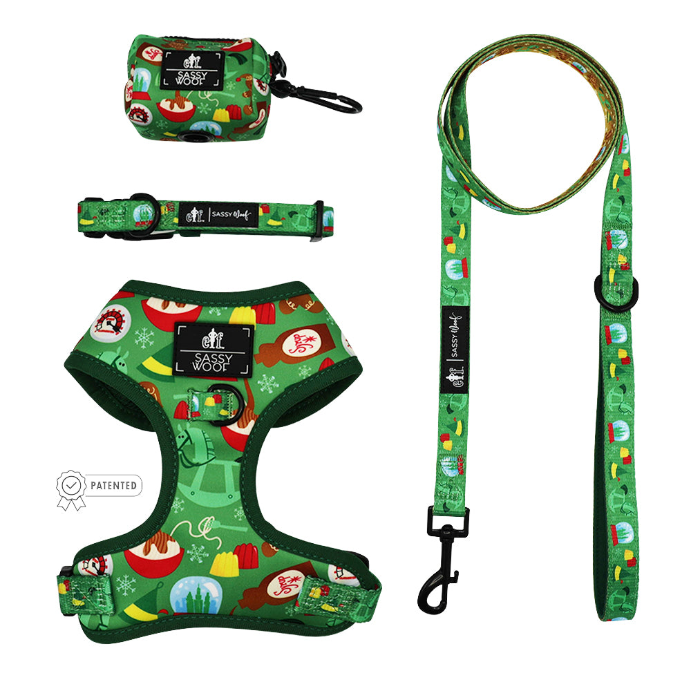 The Sassy Woof Dog Four Piece Bundle - Elf™ includes a festive green harness, collar, adjustable leash, and waste bag holder, all decorated with holiday patterns. The Sassy Woof brand is visible on every piece.