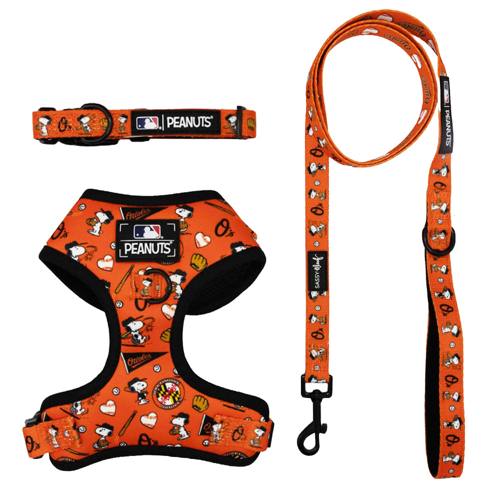 The Sassy Woof Harness Three Piece Bundle - MLB x Peanuts™ Baltimore Orioles™ includes an orange collar, adjustable harness, and leash with baseball-themed images—perfect for pups on the Puppy Growth Pawtection Plan.