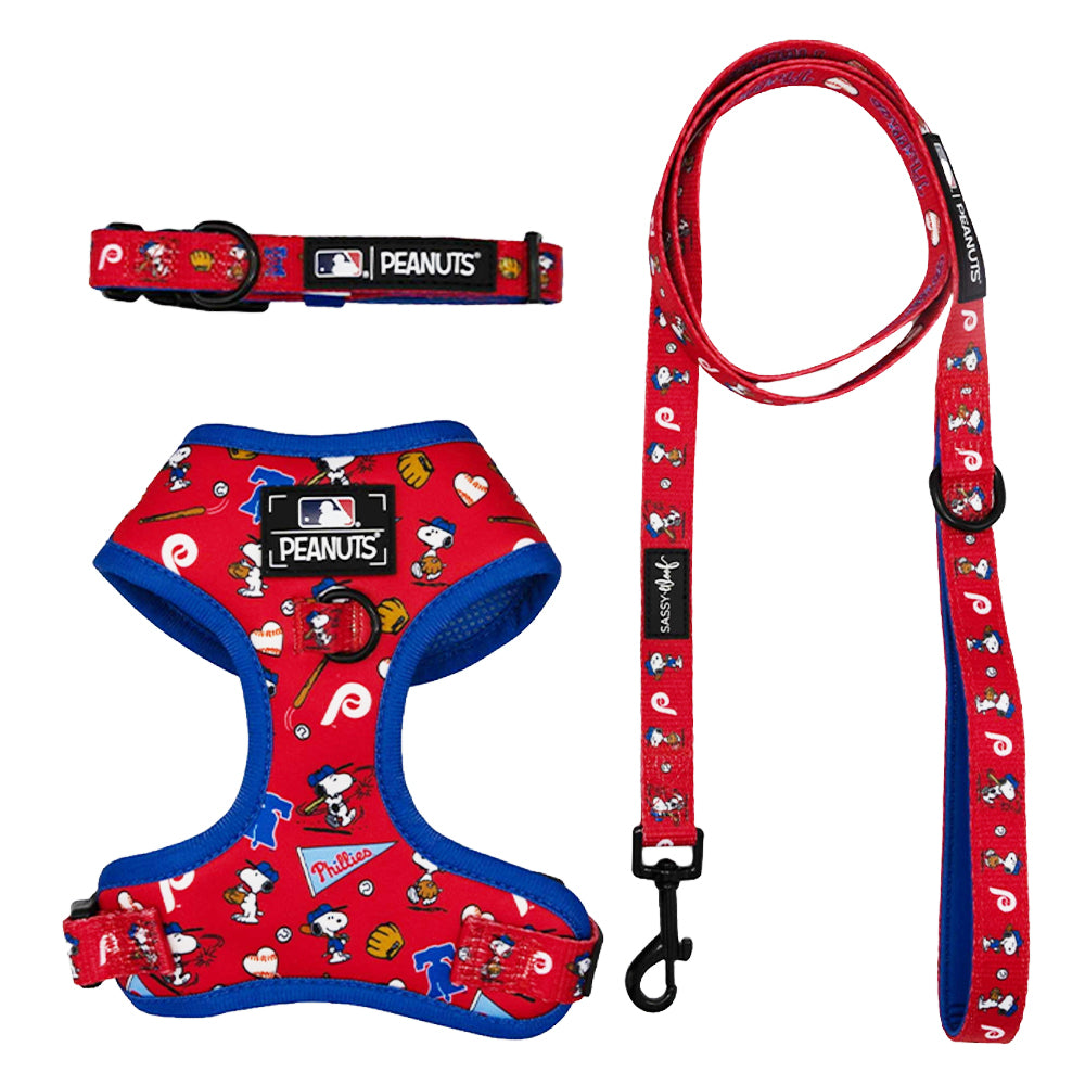 The Sassy Woof Harness Three Piece Bundle - MLB x Peanuts™ Philadelphia Phillies™ features a red and blue harness, collar, and leash with Snoopy graphics and official MLB, Phillies, and Peanuts logos.