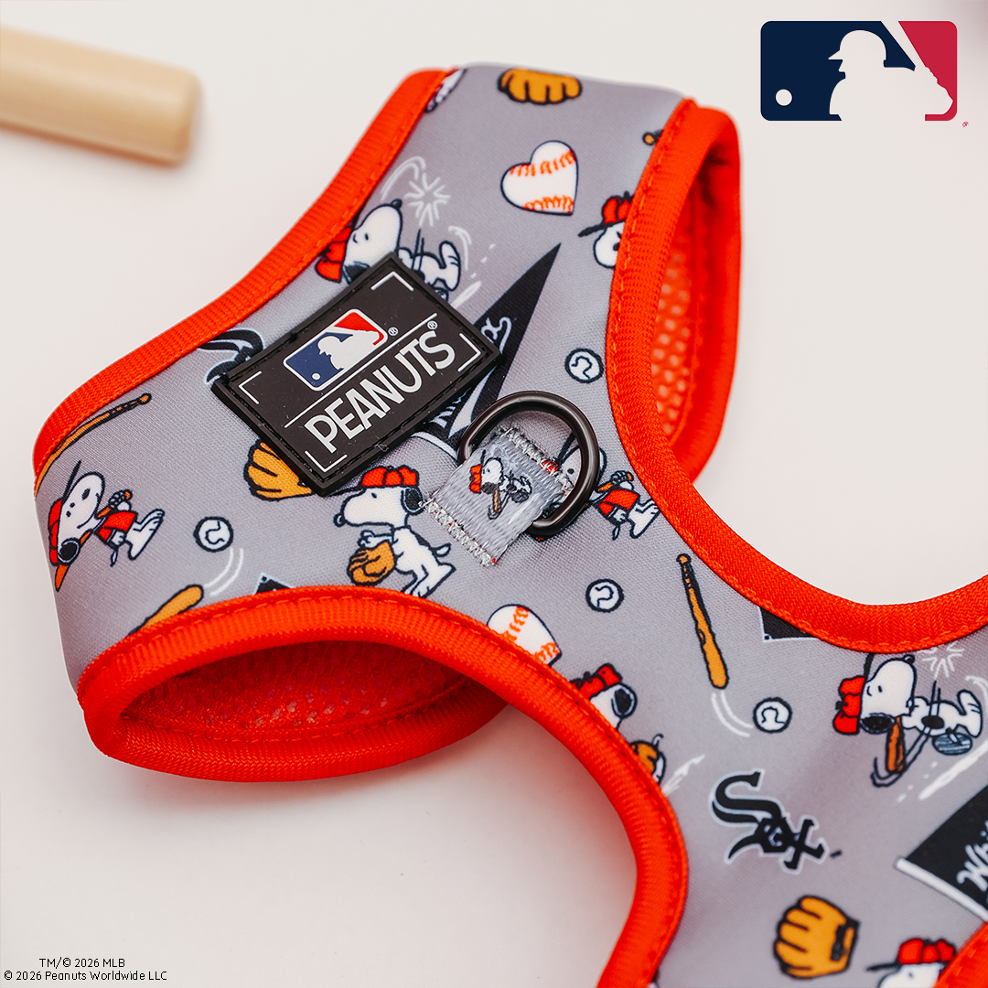 The Sassy Woof Dog Adjustable Harness - MLB™ x Peanuts™ Chicago White Sox™ features Snoopy and Woodstock playing baseball, a leash ring, and MLB and Peanuts logos, with a bat in the background and the MLB logo in the top right corner.