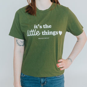 A red-haired person with tattoos stands against a plain background wearing the Human Tee - It’s the Little Things by Sassy Woof, a green, lightweight unisex 100% ring-spun cotton t-shirt, paired with blue jeans.