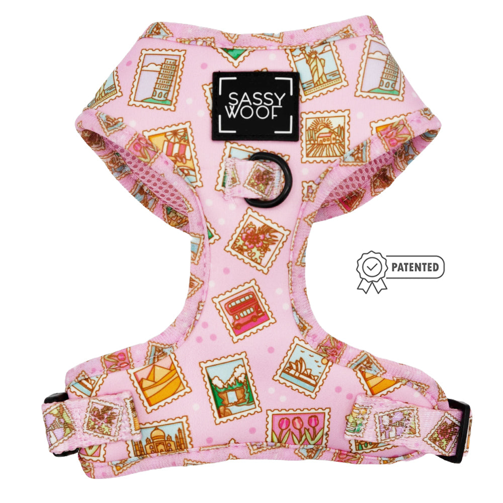 The Sassy Woof Dog Adjustable Harness - Out of Office is a pink, no-pull harness featuring postage stamp landmark prints, black hardware, adjustable straps, and a front Sassy Woof label. A Patented icon appears beside it.