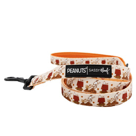 The Dog Leash - Peanuts™ Harvest by Sassy Woof features a comfy neoprene handle, playful Snoopy and red doghouse designs, a black metal clasp, vibrant orange underside, and co-branding with Peanuts.