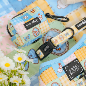 The Sassy Woof Dog Waste Bag Holder - Patch Perfect is shown on a pastel patchwork fabric with rabbits, bows, and daisies, creating a playful quilted look. White flowers are visible in the corner for added charm.