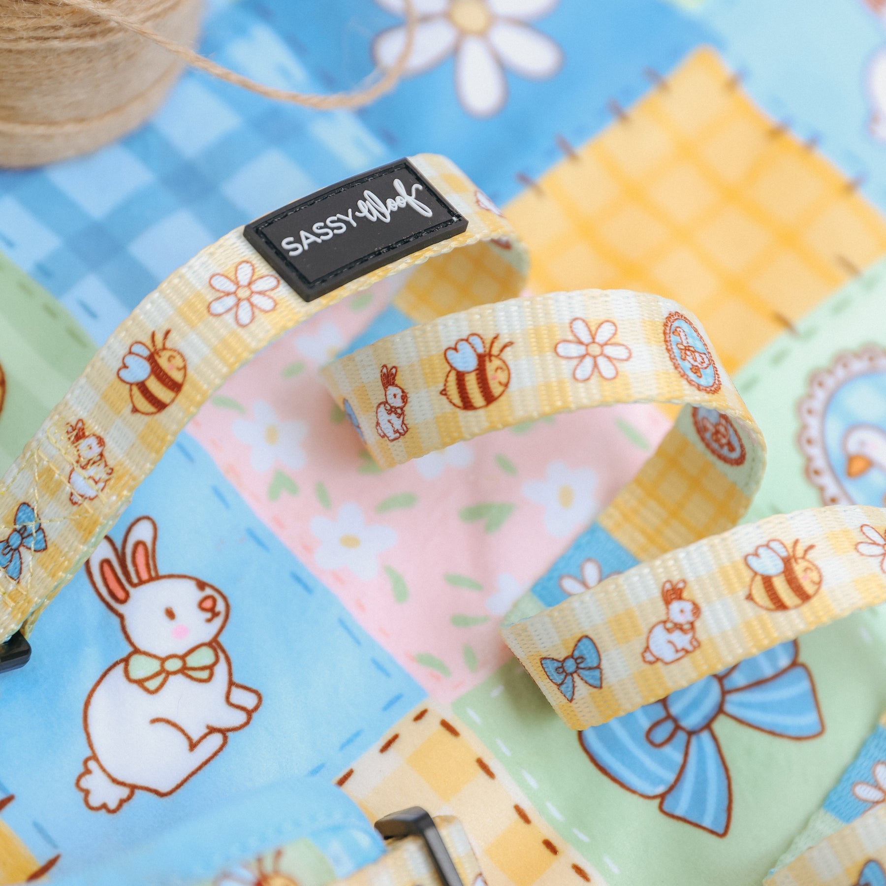 A close-up of a spring-themed fabric with cartoon bunnies, bees, flowers, and bows. The Sassy Woof Dog Leash - Patch Perfect in yellow neoprene with matching designs and label is also shown—perfect for your pup’s style!.