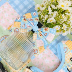 The Sassy Woof Dog Sailor Bow - Patch Perfect, in blue and pastel with cartoon animals, decorates a ribbed glass vase. White daisies above a pastel picnic-pattern cloth complete this charming, whimsical arrangement.