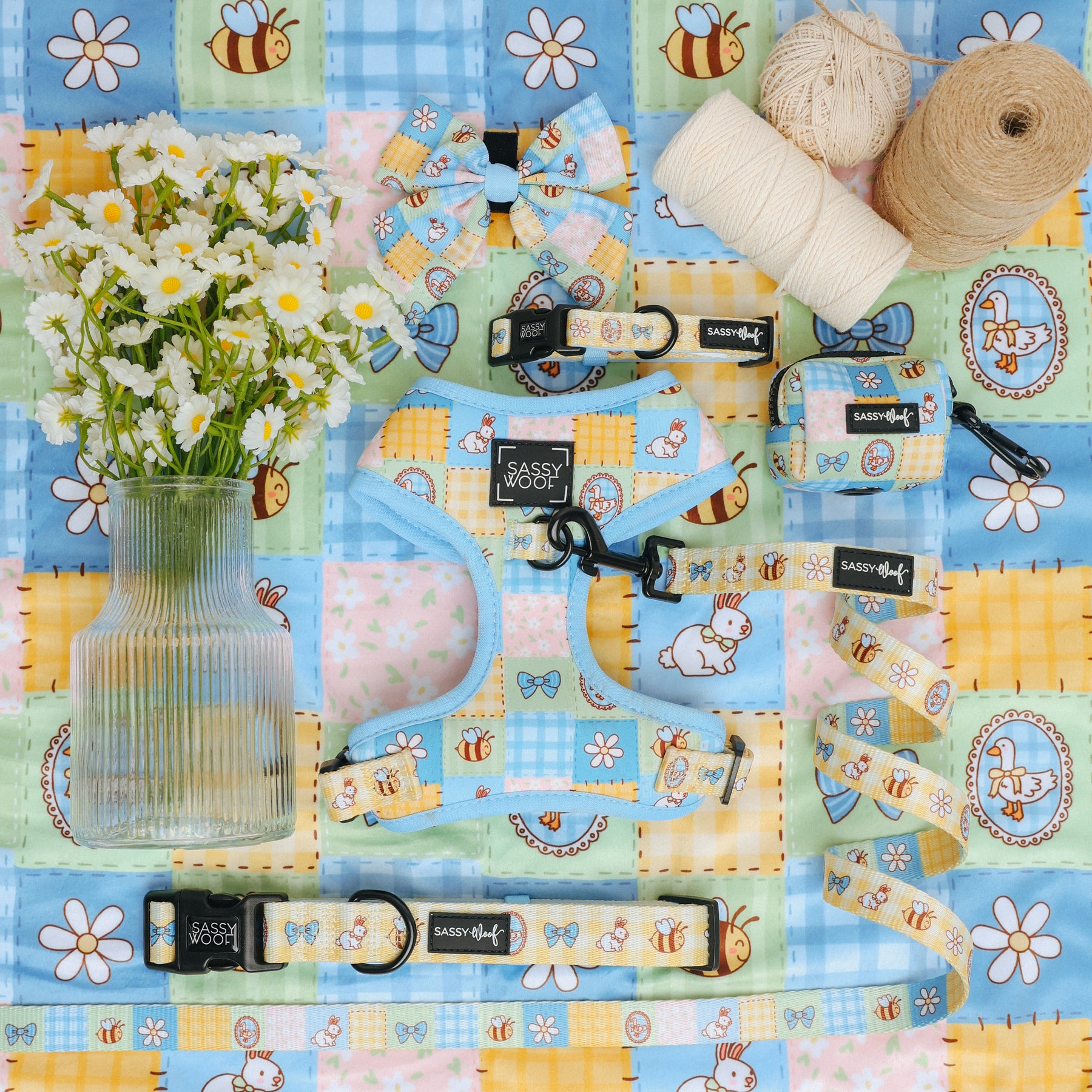 Sassy Woof’s Dog Four Piece Bundle - Patch Perfect, featuring stylish pet accessories, is picnic-pattern styled on a colorful quilt. A vase of daisies and twine complete this charming display for your pup.