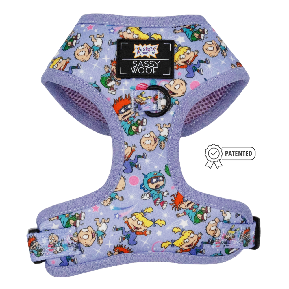 The Dog Adjustable Harness - Nickelodeon Rugrats™ by Sassy Woof features a lavender design with colorful Rugrats characters, a front Sassy Woof label, black metal leash ring, and is shown beside the Puppy Growth Pawtection Plan badge.