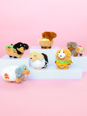 Six cute Sassy Woof stuffed Dachshund toy dogs—dressed as foods like taco, burger, hot dog, sushi, and sandwich—are displayed on white risers with a pink background. Find out which Blind Box plush keychain you’ll receive!.