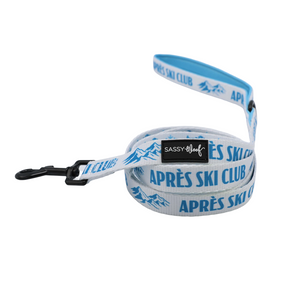 Introducing the Sassy Woof Dog Two Piece Bundle - Après Ski Club: This coordinated set includes a white leash featuring blue “APRÈS SKI CLUB” text, blue mountain graphics, and a sturdy black clip—perfectly paired with the matching harness for a unified winter look. The handle is adorned with the signature SASSY WOOF label, adding both style and functionality to your dog’s cozy ensemble.