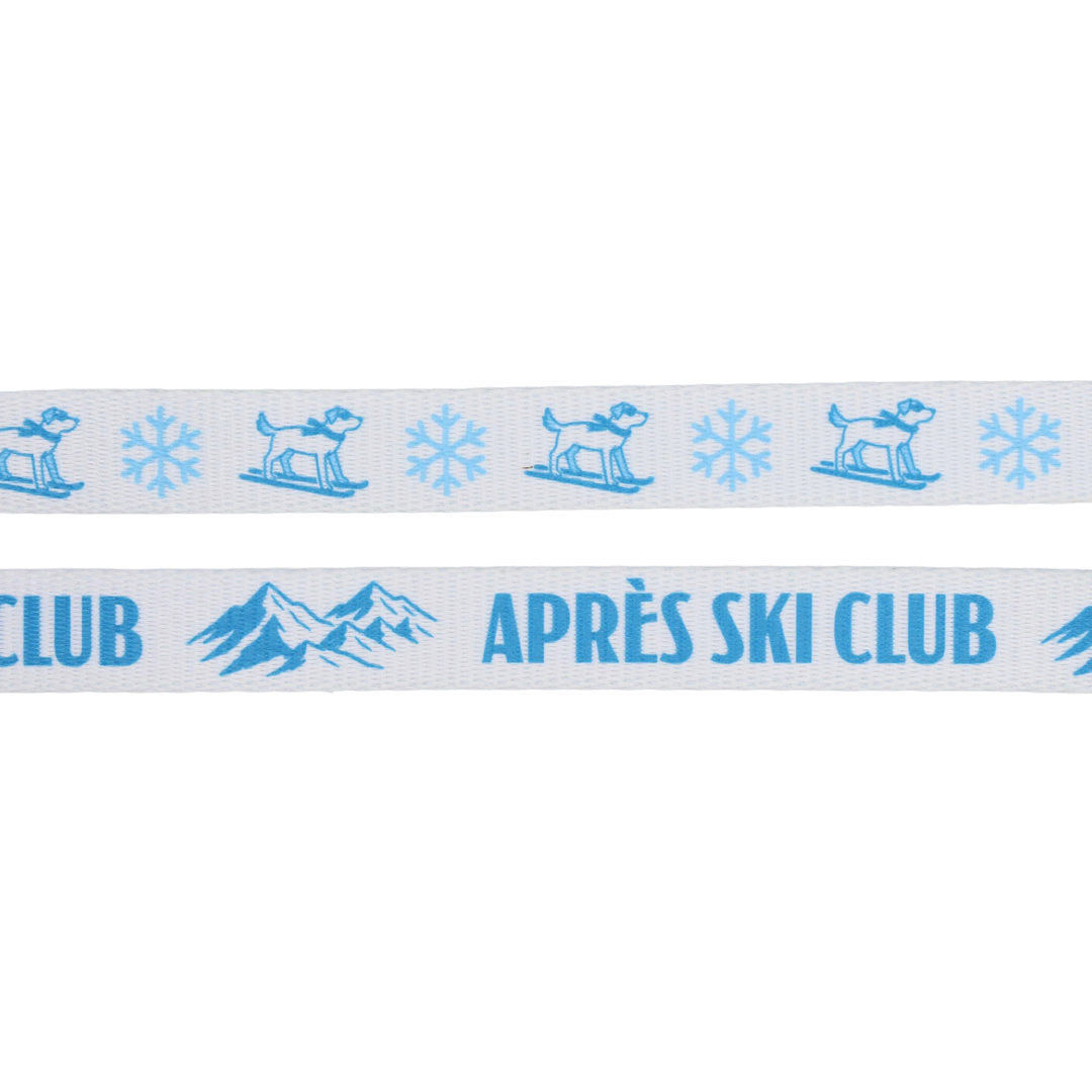 Introducing the Dog Two Piece Bundle - Après Ski Club by Sassy Woof: featuring a white ribbon adorned with blue images of a dog on skis, snowflakes, mountains, and the text “APRÈS SKI CLUB.” This charming bundle is perfect for pairing with your cozy winter dog leash or Après Ski Club dog harness. The playful design makes it a stylish accessory for any pup ready to hit the slopes or enjoy après-ski cuddles.