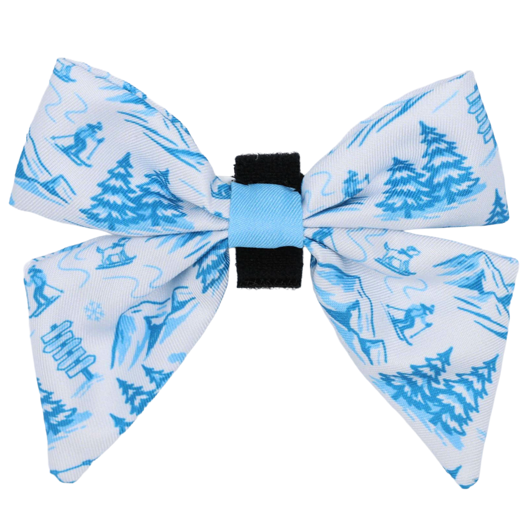 Introducing the Dog Sailor Bow - Après Ski Club by Sassy Woof—a white and blue sailor bow with a black center, adorned with a charming winter scene of trees, skiers, sleds, and snowflakes. Perfect for pairing with cozy dog collars or other winter accessories from the Après Ski Club collection.