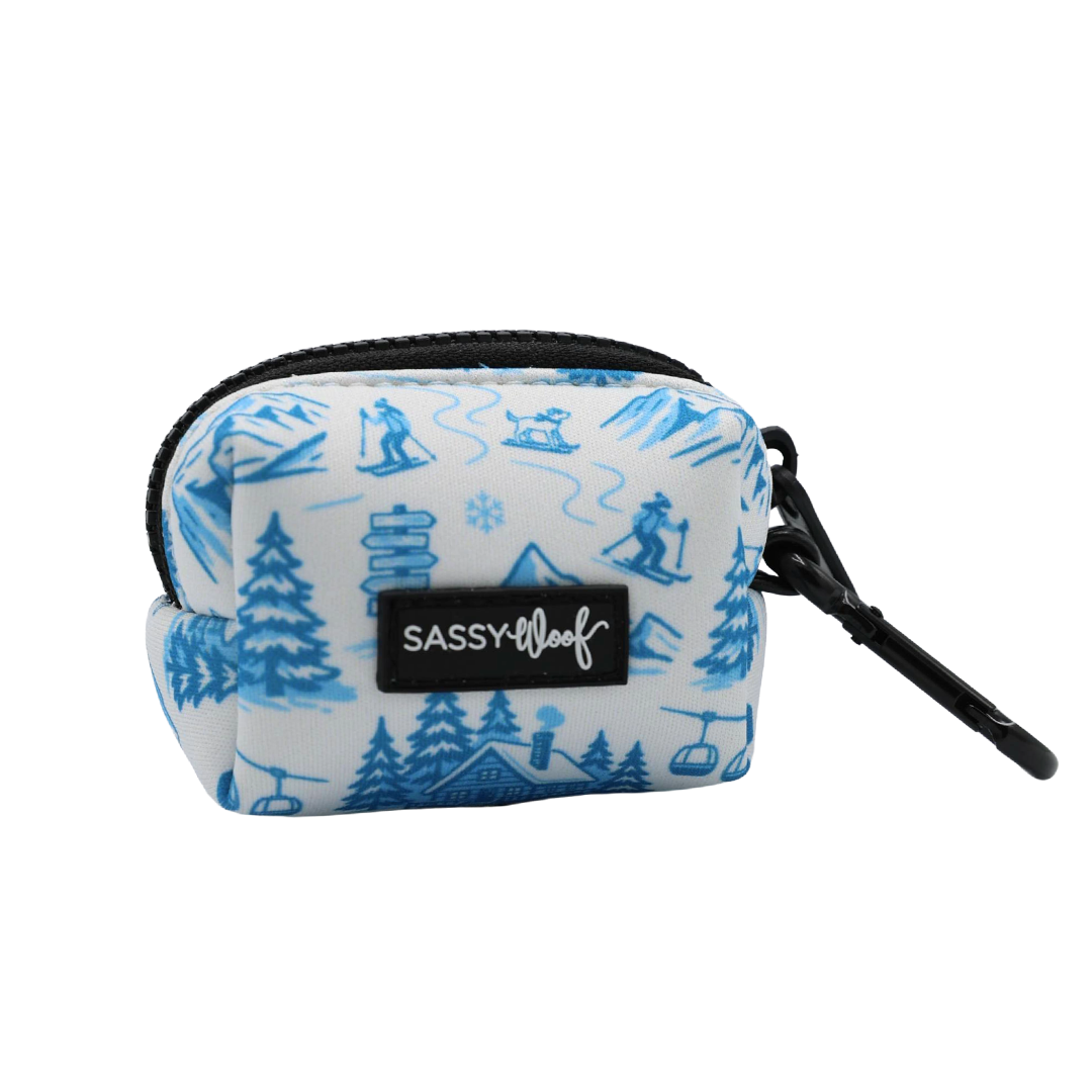 Introducing the Sassy Woof Dog Waste Bag Holder - Après Ski Club: a small white neoprene bag holder featuring blue winter-themed illustrations, completed with a black zipper, black clip, and the signature SASSY WOOF label on the front—making it the perfect Apres Ski accessory for your pup’s winter dog fashion.