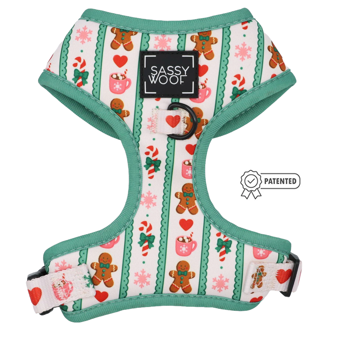 A festive adjustable harness from the Sassy Woof Dog Four Piece Bundle – Cocoa & Cookies collection, decorated with gingerbread men, candy canes, snowflakes, and hearts on vibrant green trim. The harness features a SASSY WOOF label and displays a PATENTED badge to the right—an ideal holiday accessory for dog lovers.