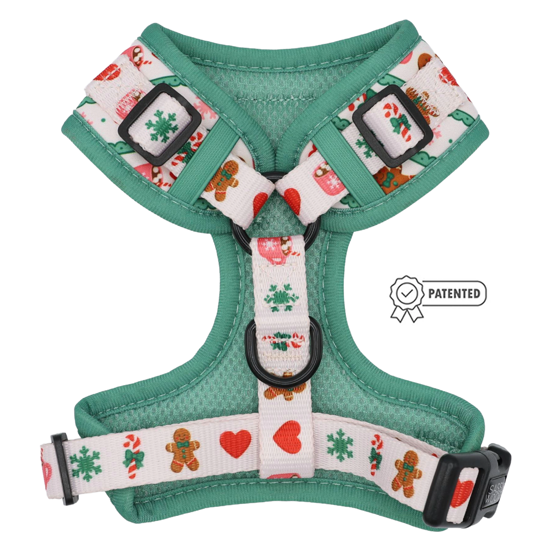 The Sassy Woof Dog Adjustable Harness - Cocoa & Cookies is a green and white custom printed neoprene harness featuring festive patterns like gingerbread men, snowflakes, hearts, and candy canes. This holiday harness includes a patented symbol displayed to the right of the harness.