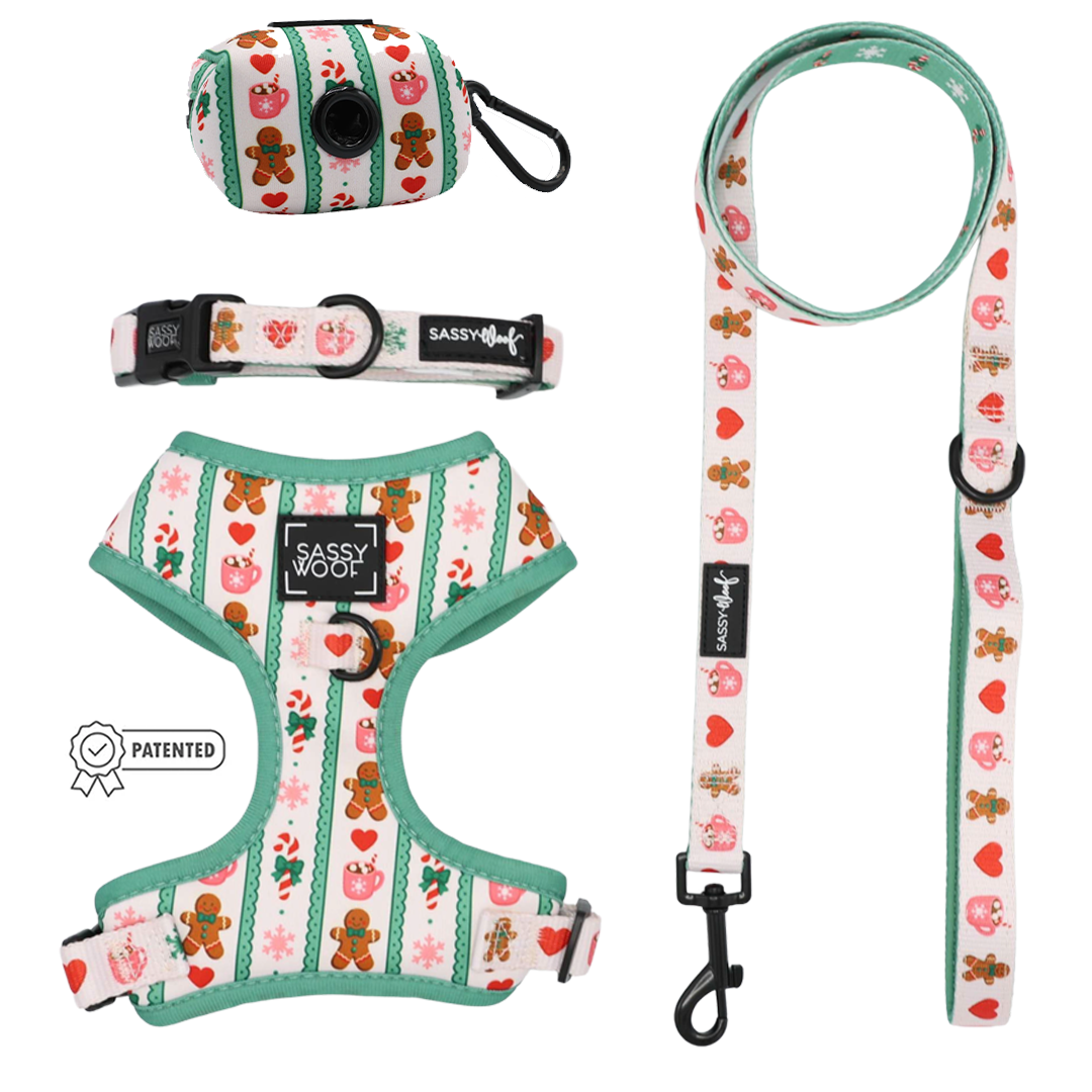 Celebrate the season with the Dog Four Piece Bundle - Cocoa & Cookies from Sassy Woof. This festive set includes a dog harness, leash, collar, and waste bag holder, all adorned with green trim and a charming pattern of gingerbread men, hearts, and holiday icons. The adjustable harness features an eye-catching Sassy Woof label for added holiday flair.