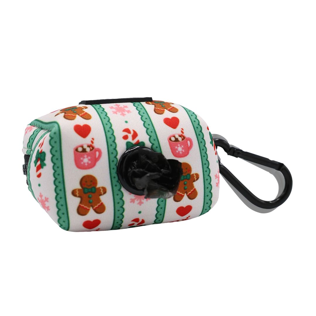 Introducing the Sassy Woof Dog Waste Bag Holder - Cocoa & Cookies: a rectangular bag holder from the festive Cocoa & Cookies collection. It features green and pink stripes with charming gingerbread and mug accents, a black plastic clip for easy attachment, and an opening on one side for convenient access to bags. Perfectly coordinates with your adjustable harness for stylish walks.