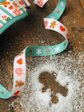 A Dog Leash from Sassy Woof’s Cocoa & Cookies collection, decorated with gingerbread men, hearts, and snowflakes, lies on a wooden surface sprinkled with white sugar and displays a gingerbread man shape in the sugar.