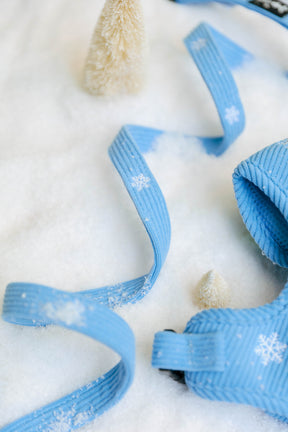 Sassy Woof Morning Frost dog leash and matching adjustable harness with white snowflake patterns lying on a snowy surface with two small bottle brush trees.