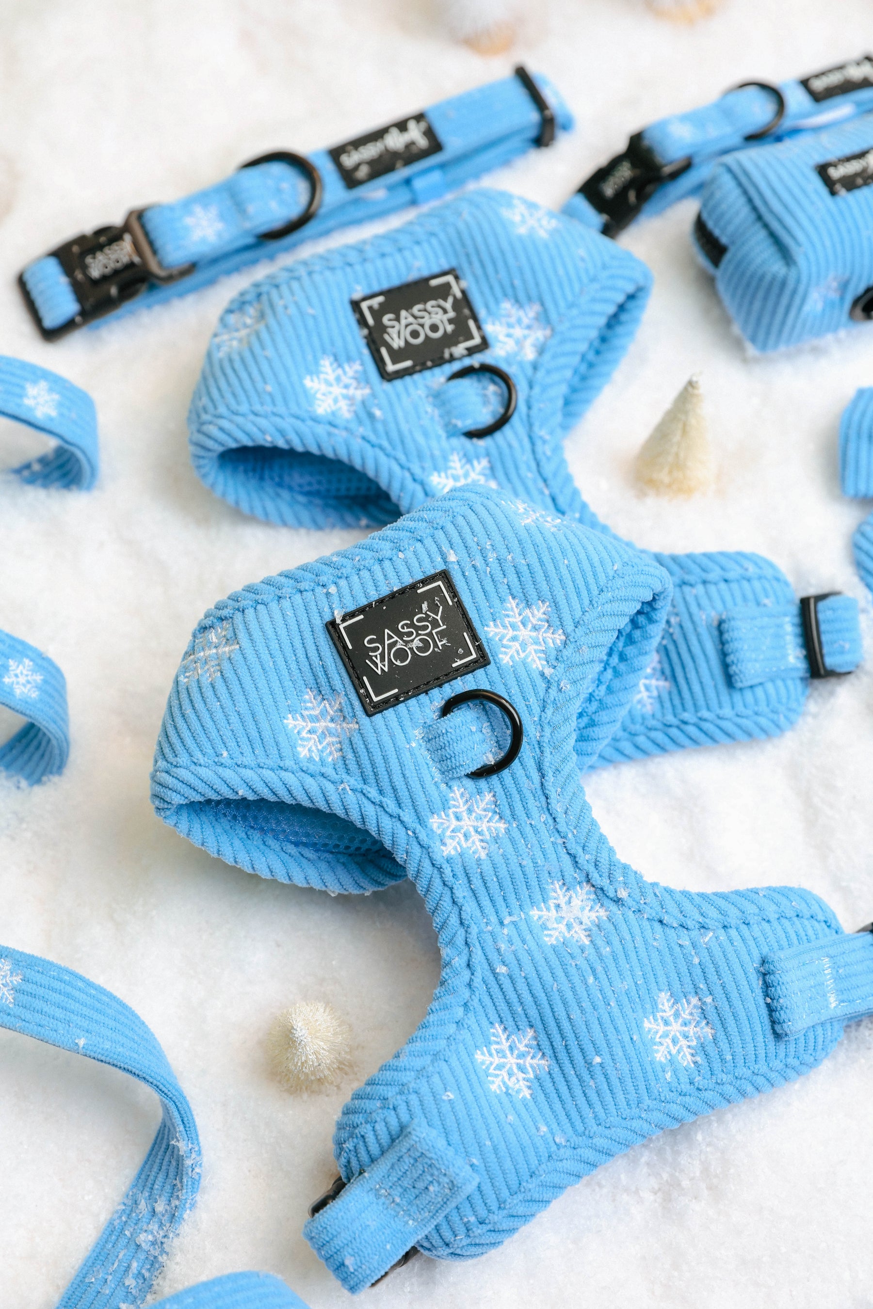 Sassy Woof Dog Four Piece Bundle - Morning Frost featuring a light blue adjustable harness, collar, and leash set with a white snowflake pattern, displayed on a snowy surface.