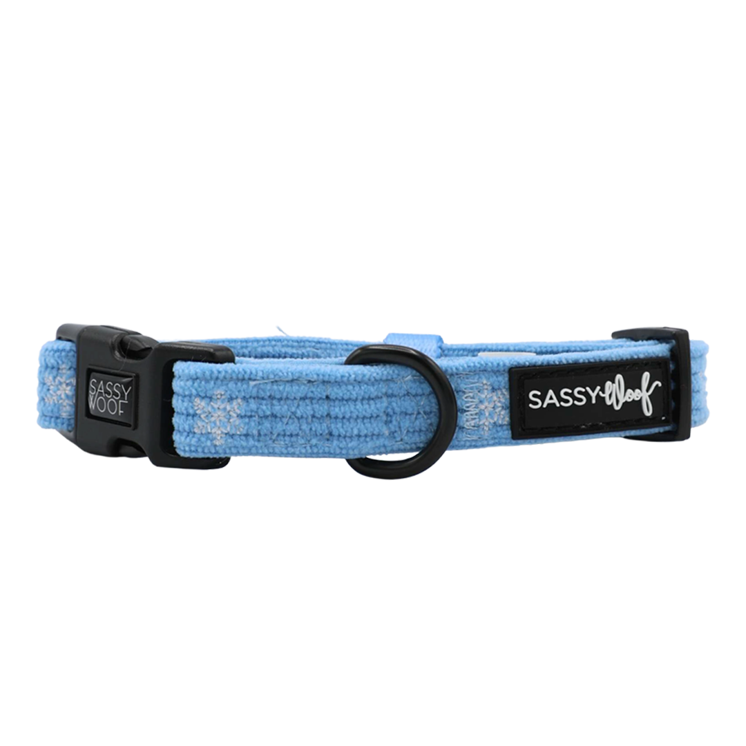 Sassy Woof Dog Collar - Morning Frost, an adjustable light blue collar featuring a repeating white snowflake pattern with black plastic buckles and a metal D-ring.