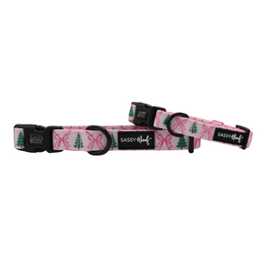 Two Pretty in Pine adjustable pink dog collars from Sassy Woof, each featuring black buckles. These collars are adorned with green Christmas tree and pink ribbon designs, making them the perfect winter accessory for your dog. The “Sassy Woof” brand name appears on a black label on each collar.