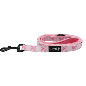 Introducing the Sassy Woof Dog Leash - Pretty in Pine: a pink leash with a black metal clip, decorated with a repeating ribbon pattern and finished with a signature Sassy Woof label sewn on the side—an ideal accessory to pair with your favorite evergreen dog collar or to mix and match with other winter dog accessories.